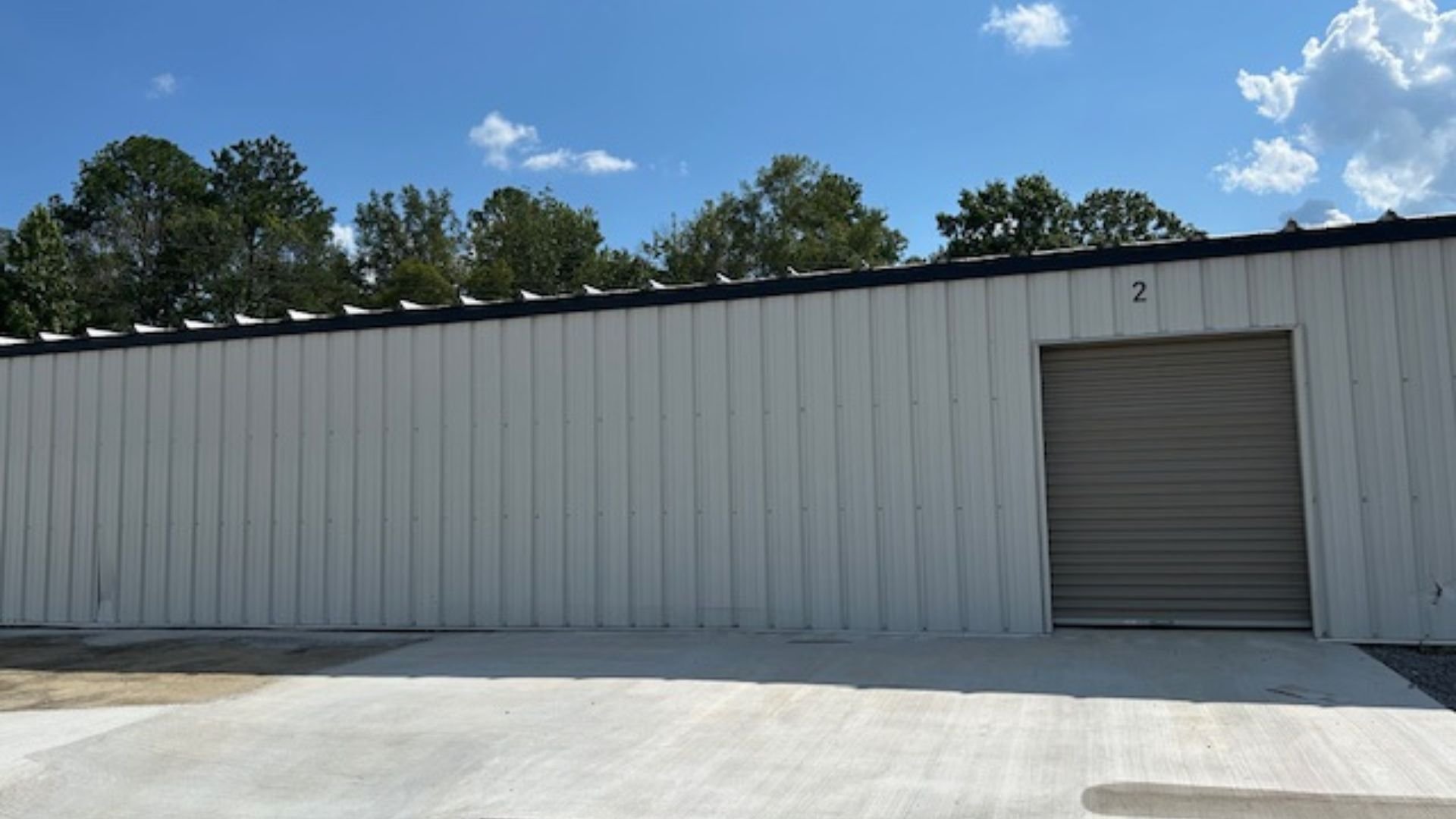 Gray metal storage unit with rollup door under blue sky with trees
