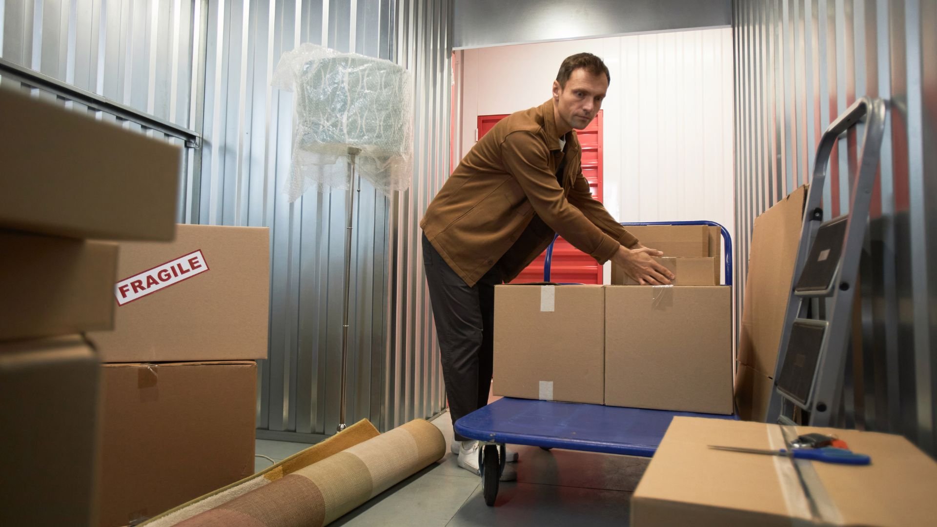 Person moving fragile boxes in a storage unit with blue cart