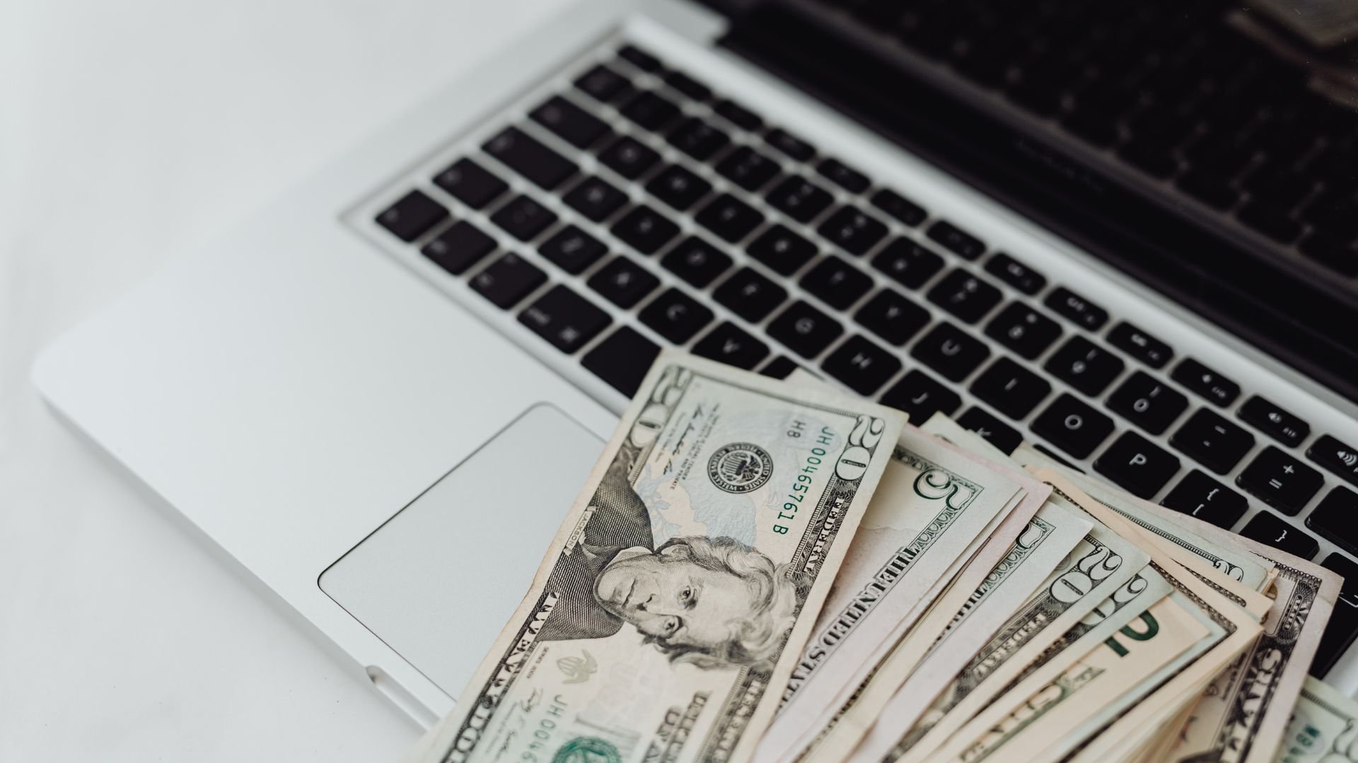 US dollar bills spread on laptop keyboard, suggesting online earnings