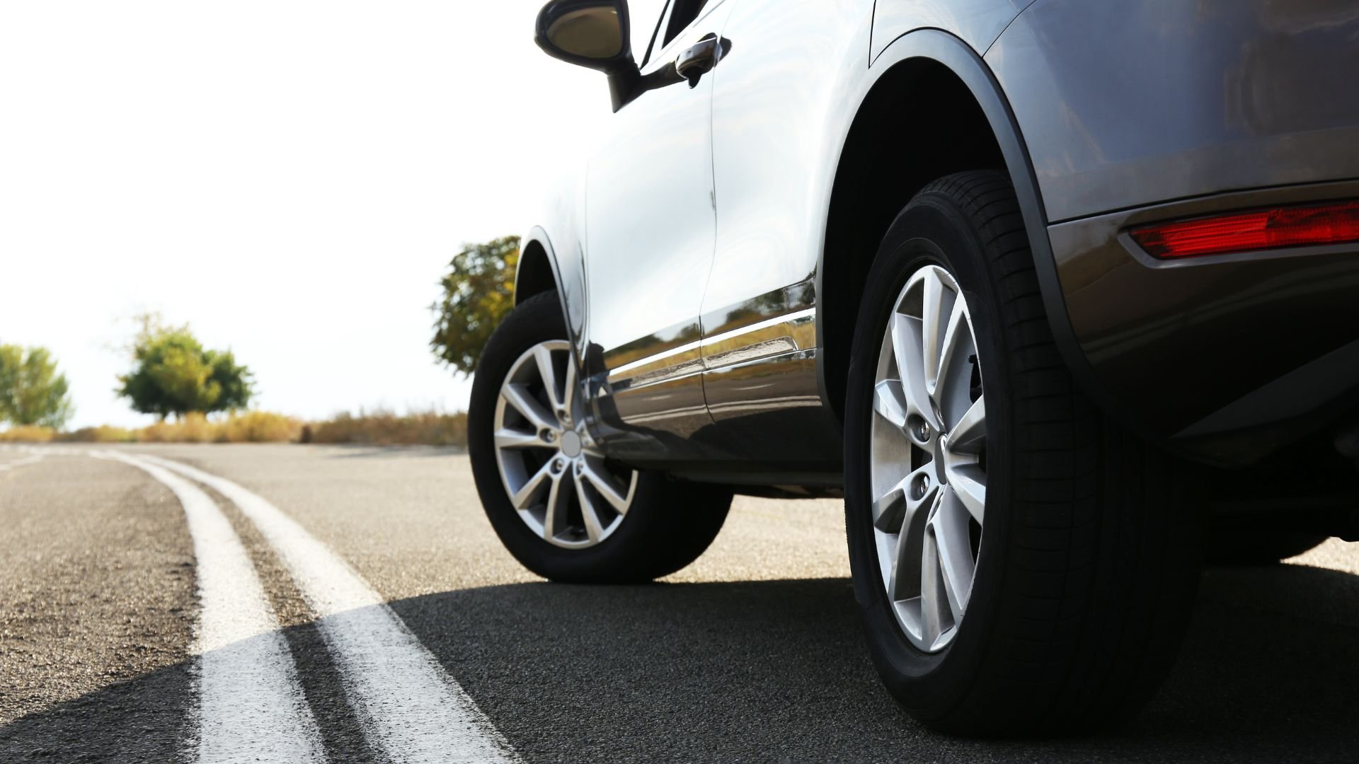 White SUV parked on road with white lines and trees in background
