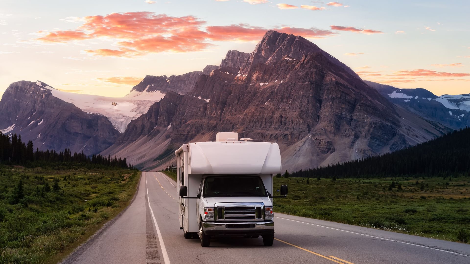 RV driving on mountain road during scenic sunset with rocky peaks