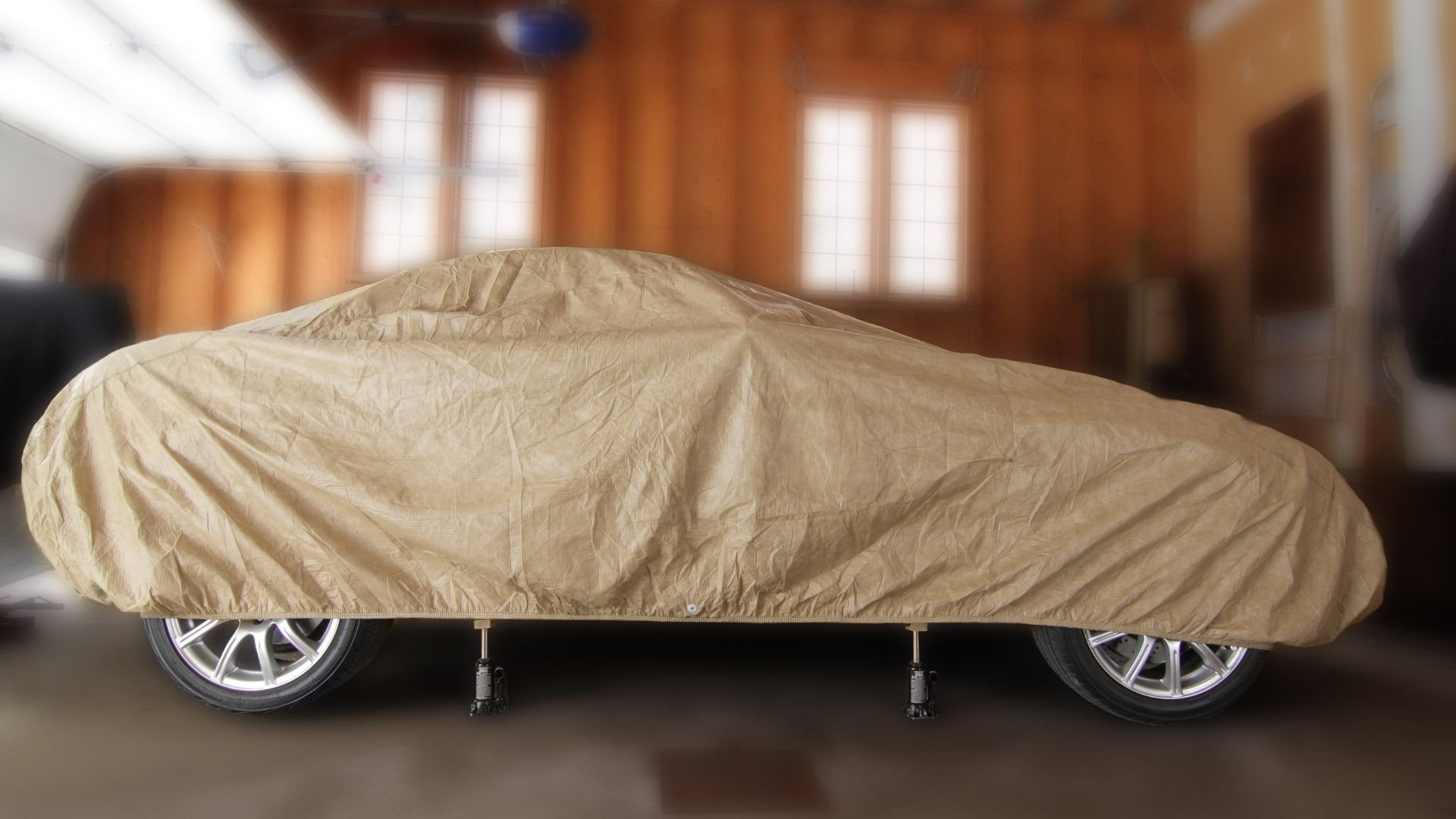 Beige car cover protecting vehicle in wooden-walled indoor space