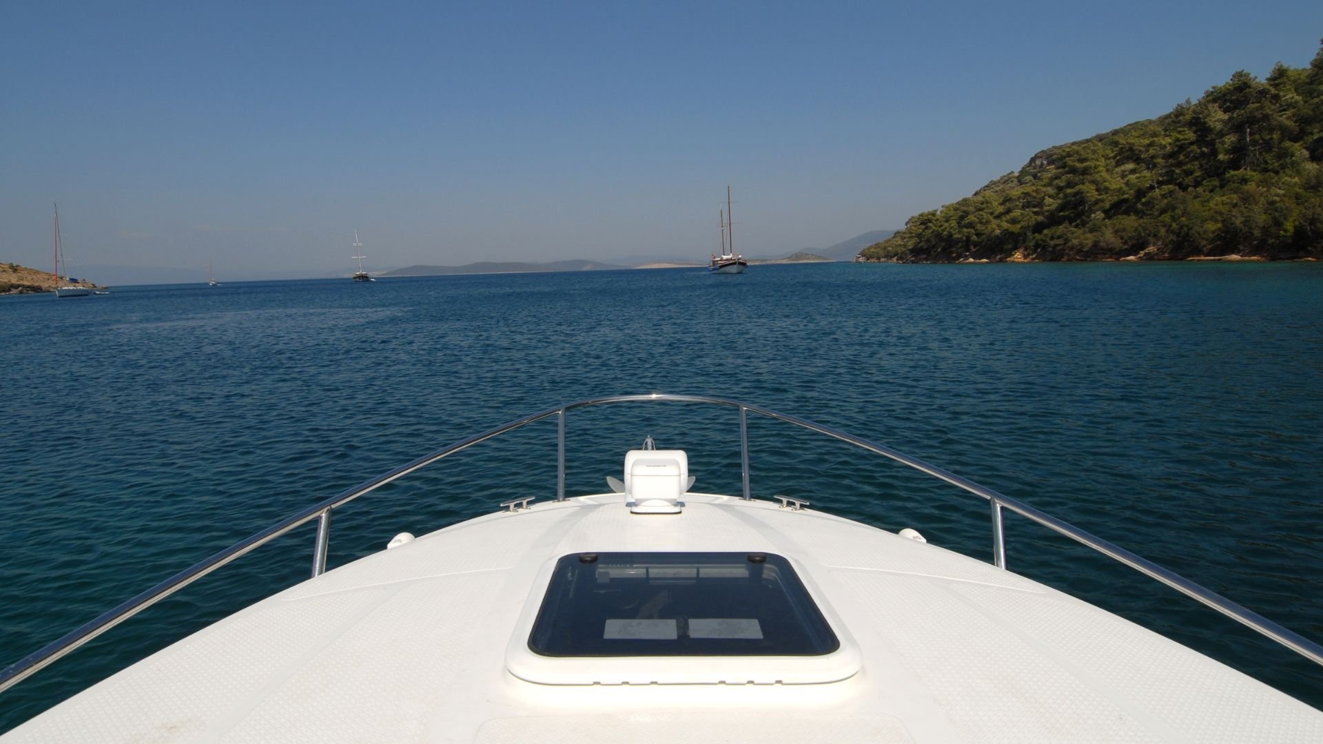 White boat bow sailing in calm blue sea with sailboats and green island