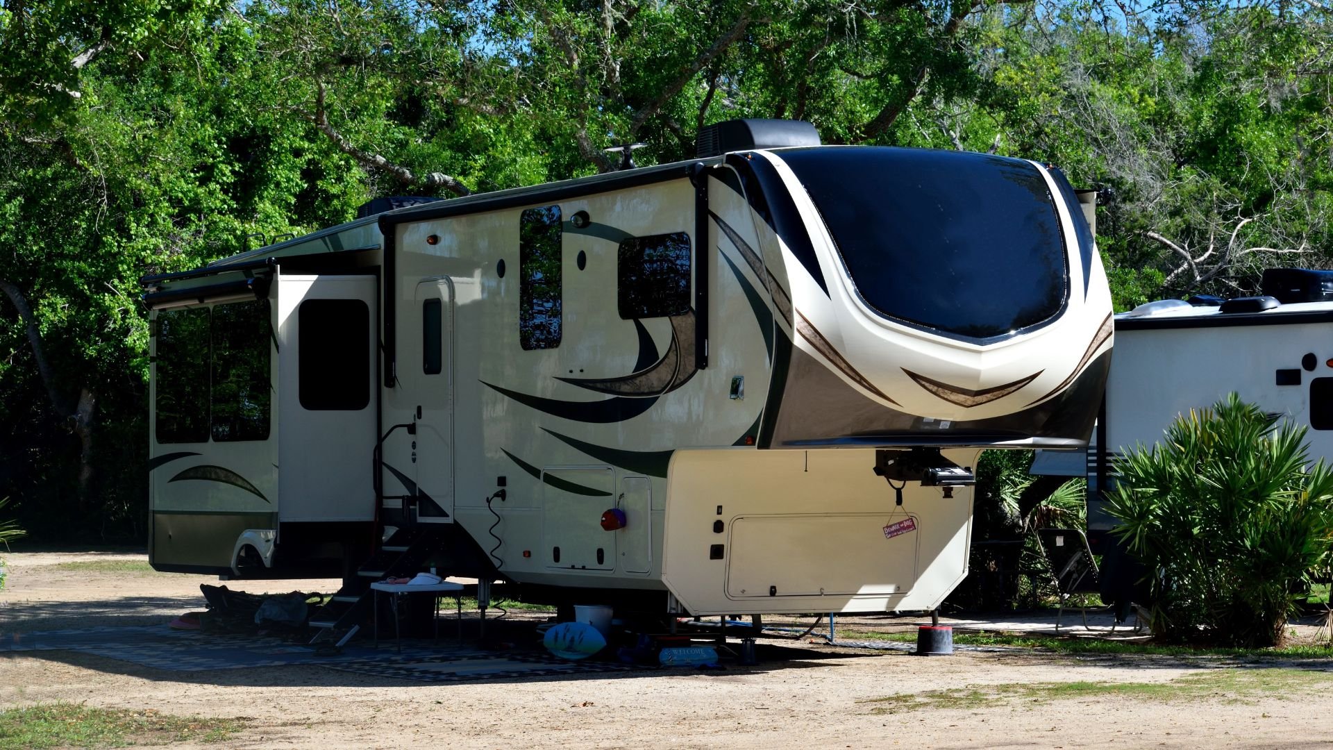Modern white and black fifth-wheel trailer parked in a green campground