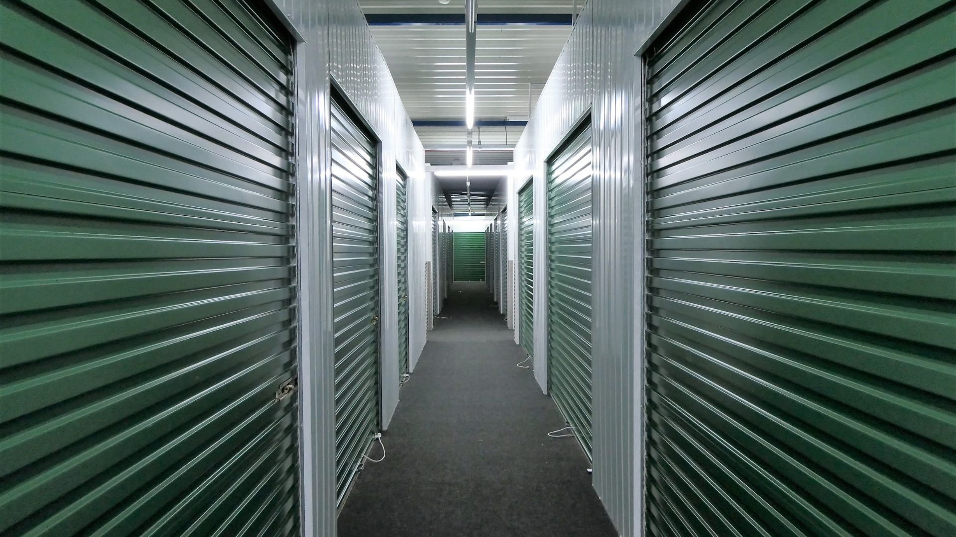 Green and white storage unit hallway with rows of locked doors