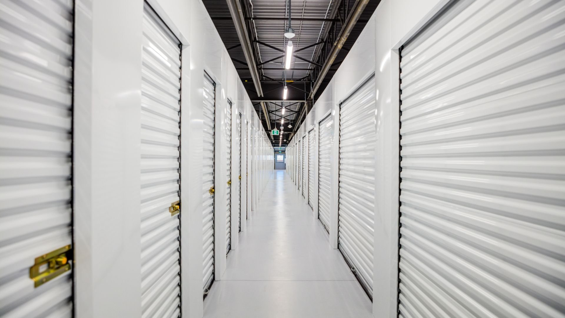White storage unit hallway with rows of closed lockers and overhead lighting