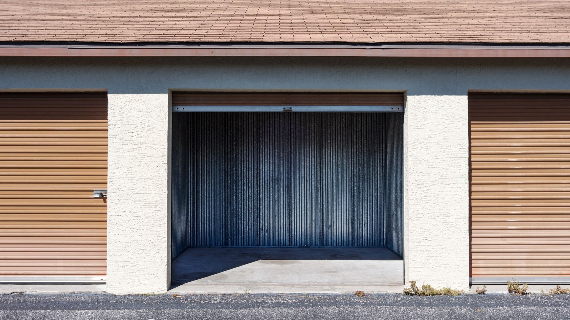 Open empty storage unit with brown doors in a white and tan building