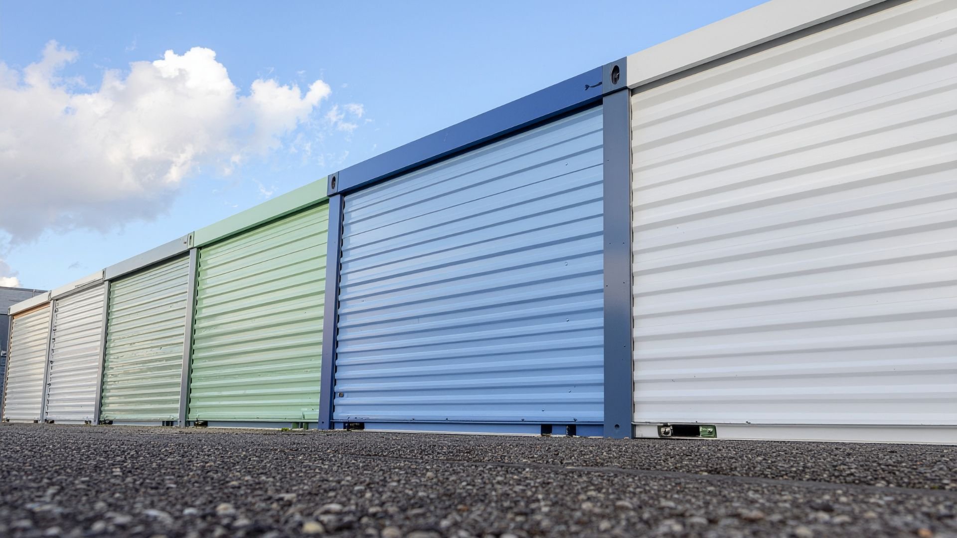 Storage units in different colors with rolled metal doors on asphalt