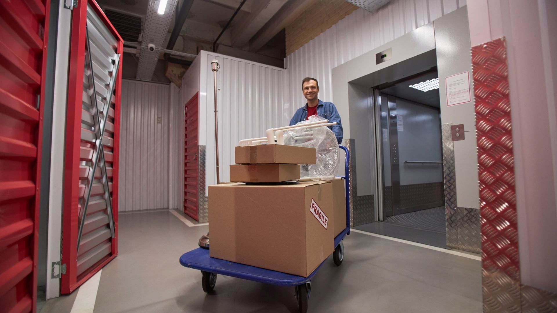 Person with cart of fragile boxes near elevator in storage facility
