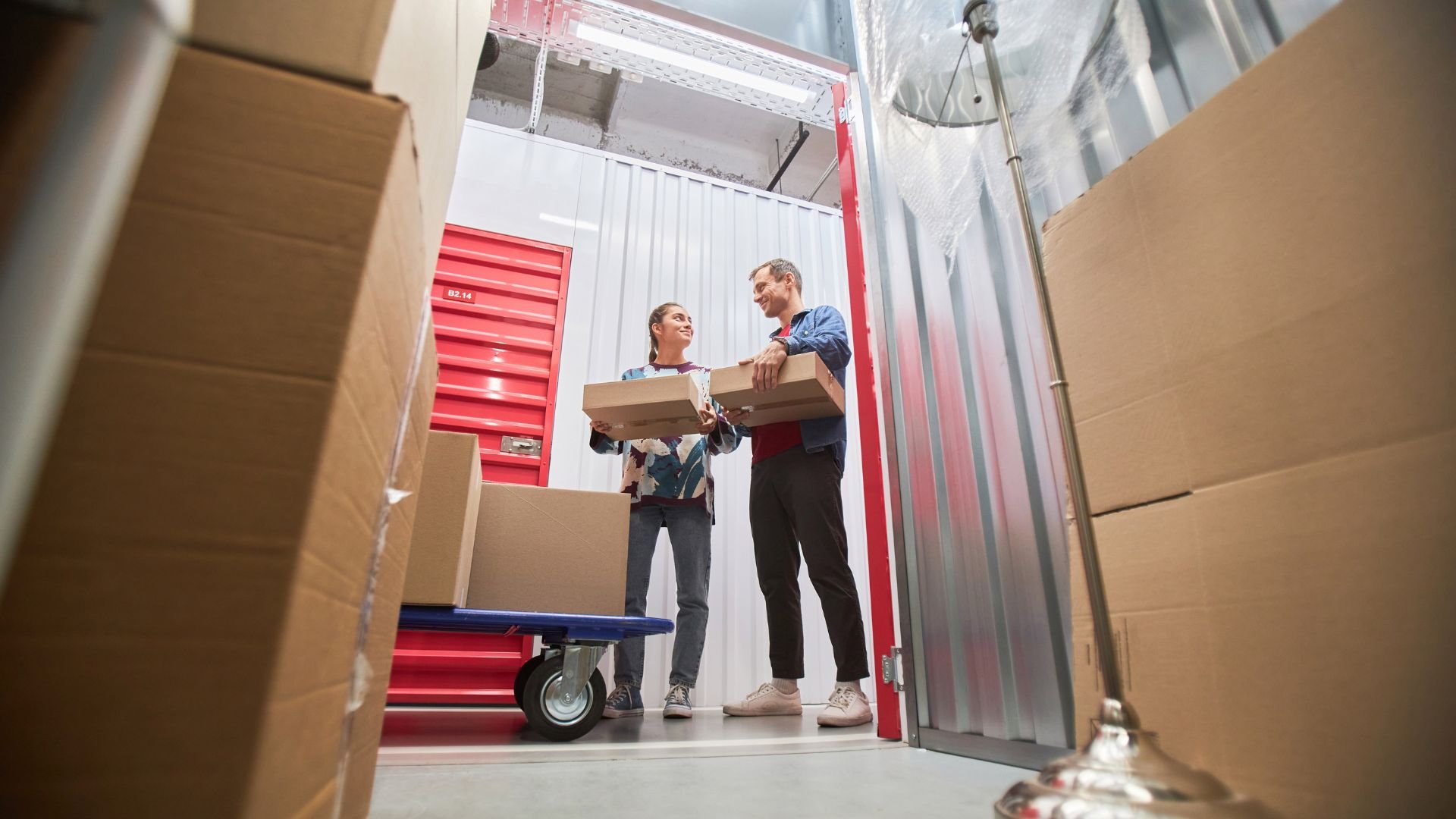 Two people moving boxes in a storage unit with red lockers